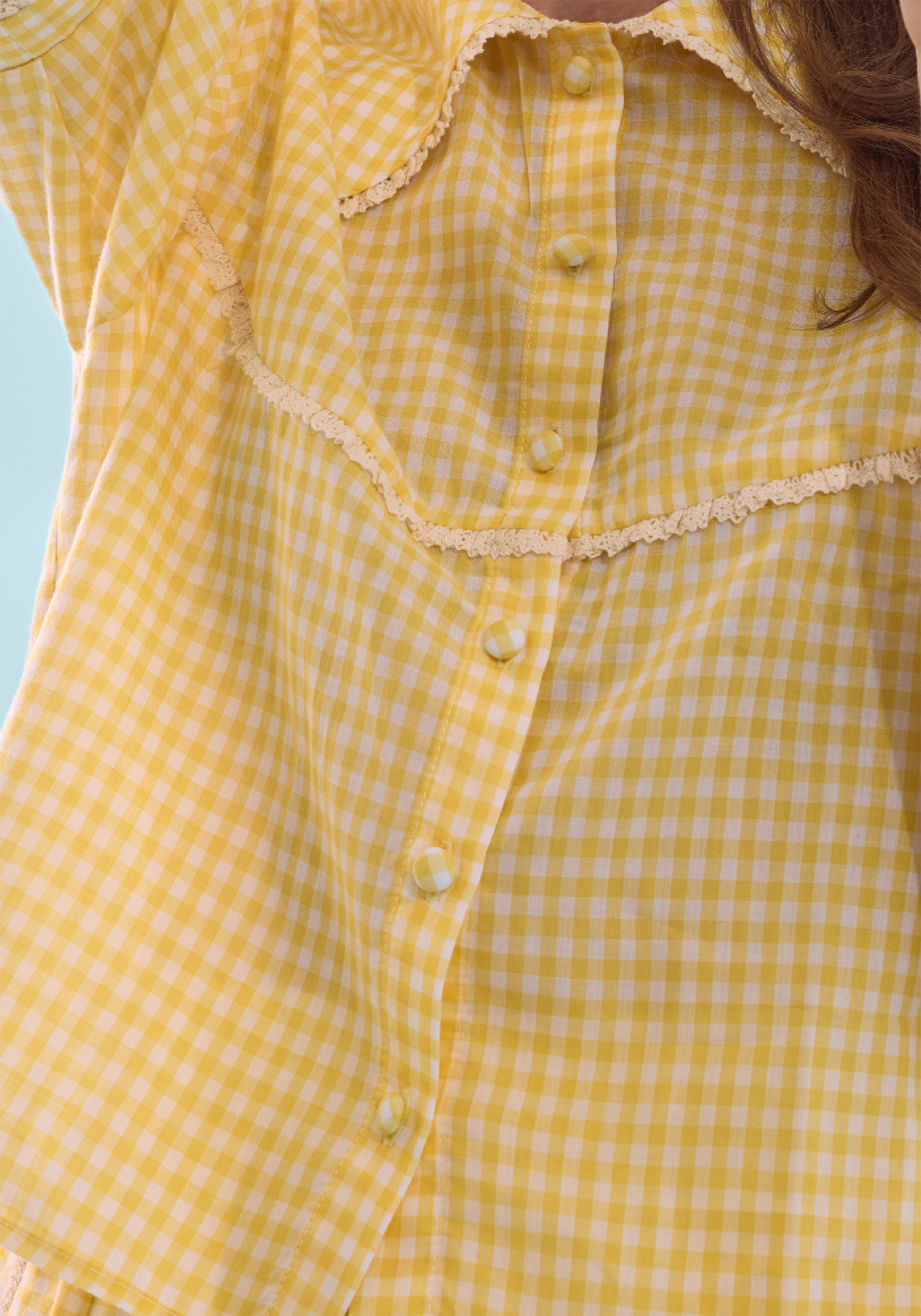 Close-up yellow gingham PJ shirt with lace trim on a light blue background