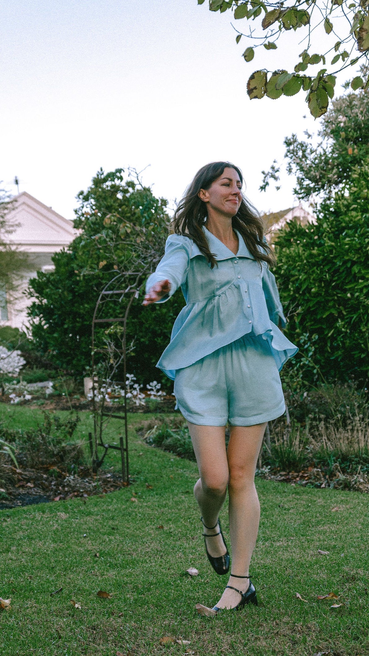 Young lady in an ice blue vintage-inspired pyajama set skipping in a garden