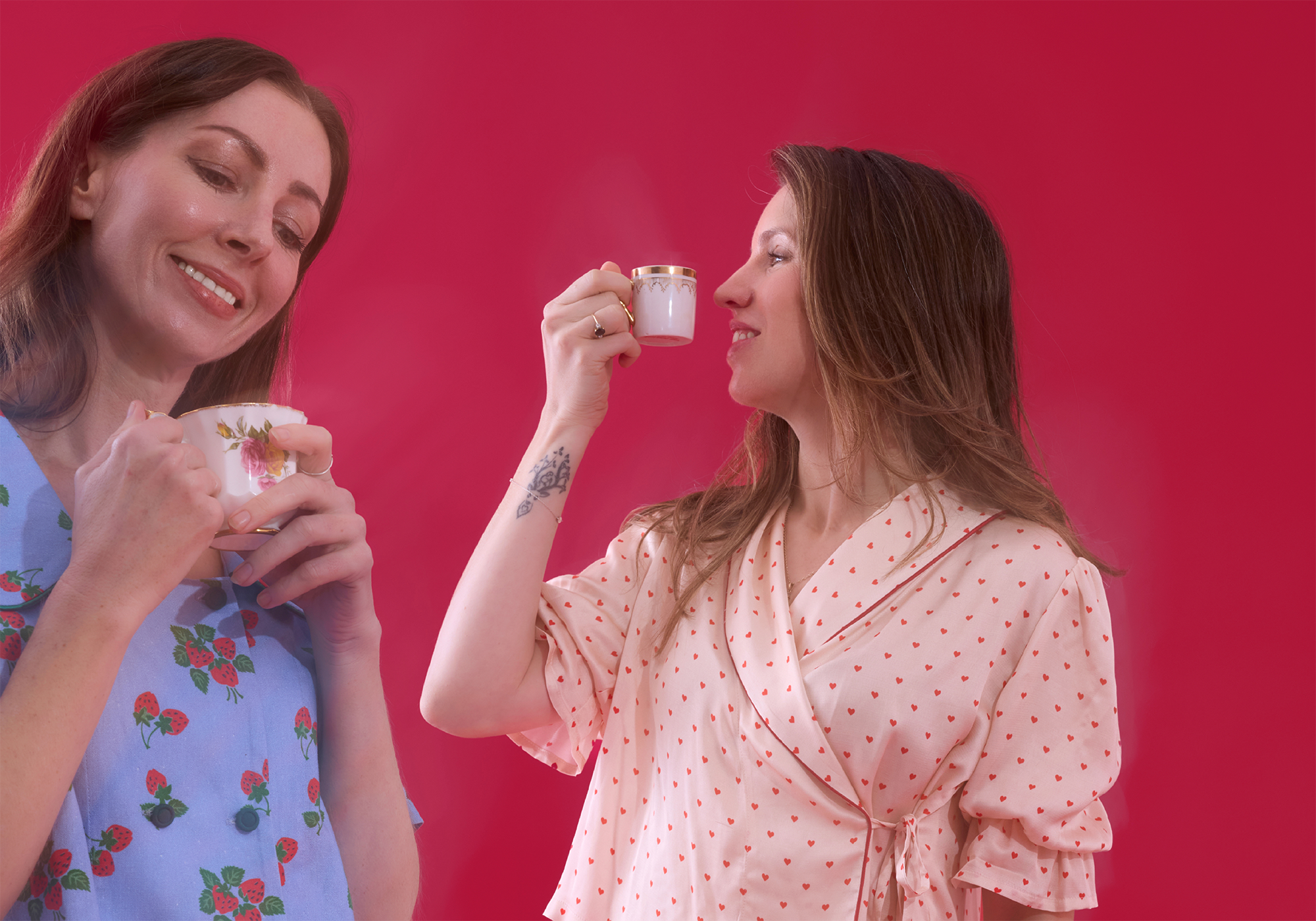 two women standing in pyjama sets drinking cups of tea and smiling