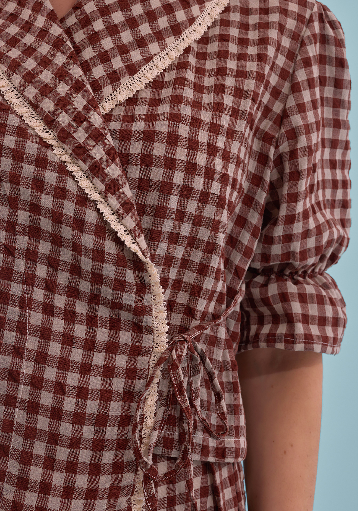 Close-up of brown and cream gingham PJ top with lace trim detail on blue background