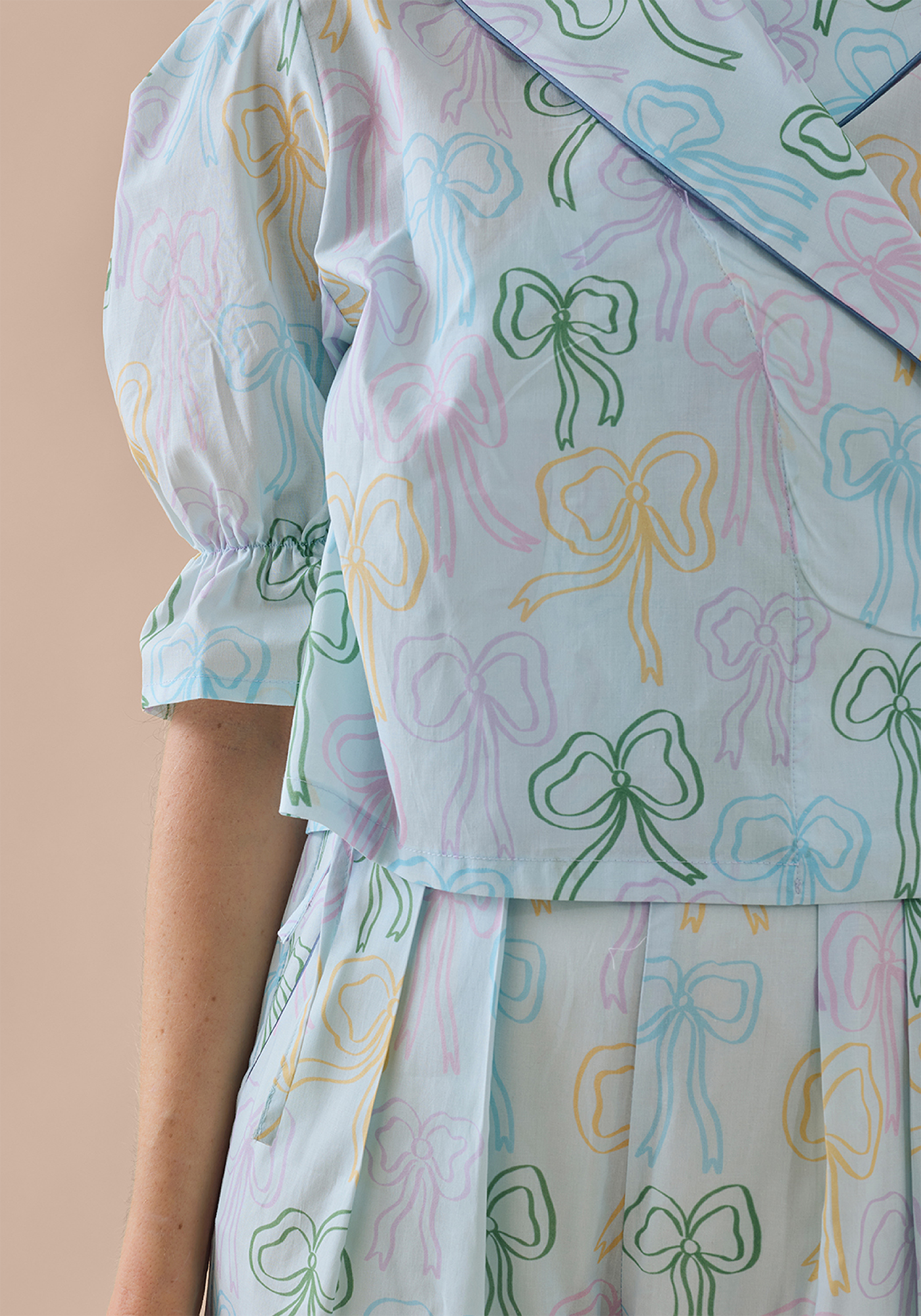 Close up of pale blue PJ set with pastel bow pattern on beige background 